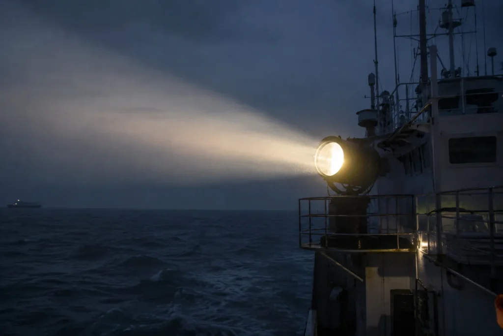 Marine searchlights are glowing on the ship.